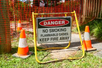A warning sign relating to a gas leak placed on a footpath in the northern beaches suburb of Fairlight, Sydney.  A plastic fence has been erected around the site.  This image was taken on a bright afternoon in summer.